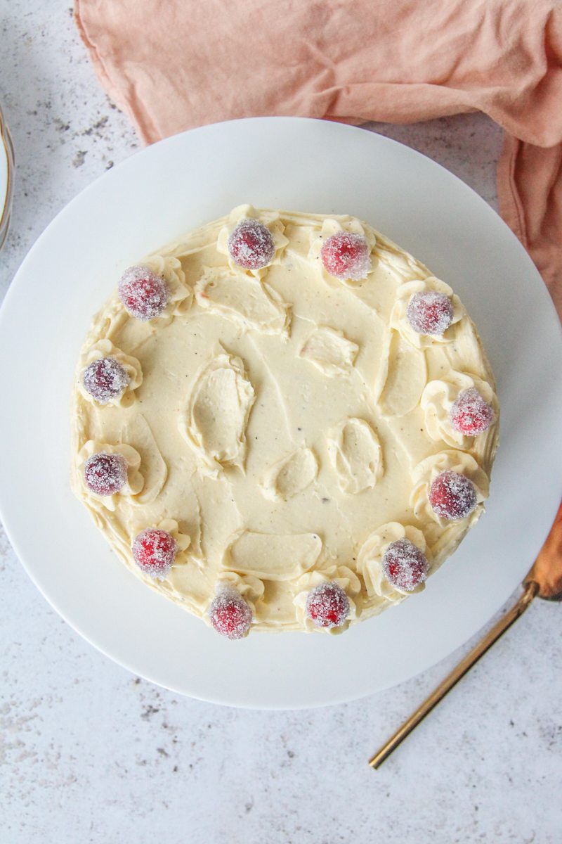 A orange cranberry layer cake sits on a white ceramic plate on a light gray surface.