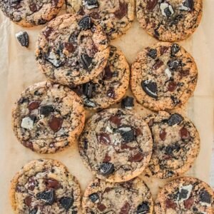 Oreo chocolate chip cookies is about to be picked up from a cooling rack lined with parchment paper on a light gray surface.