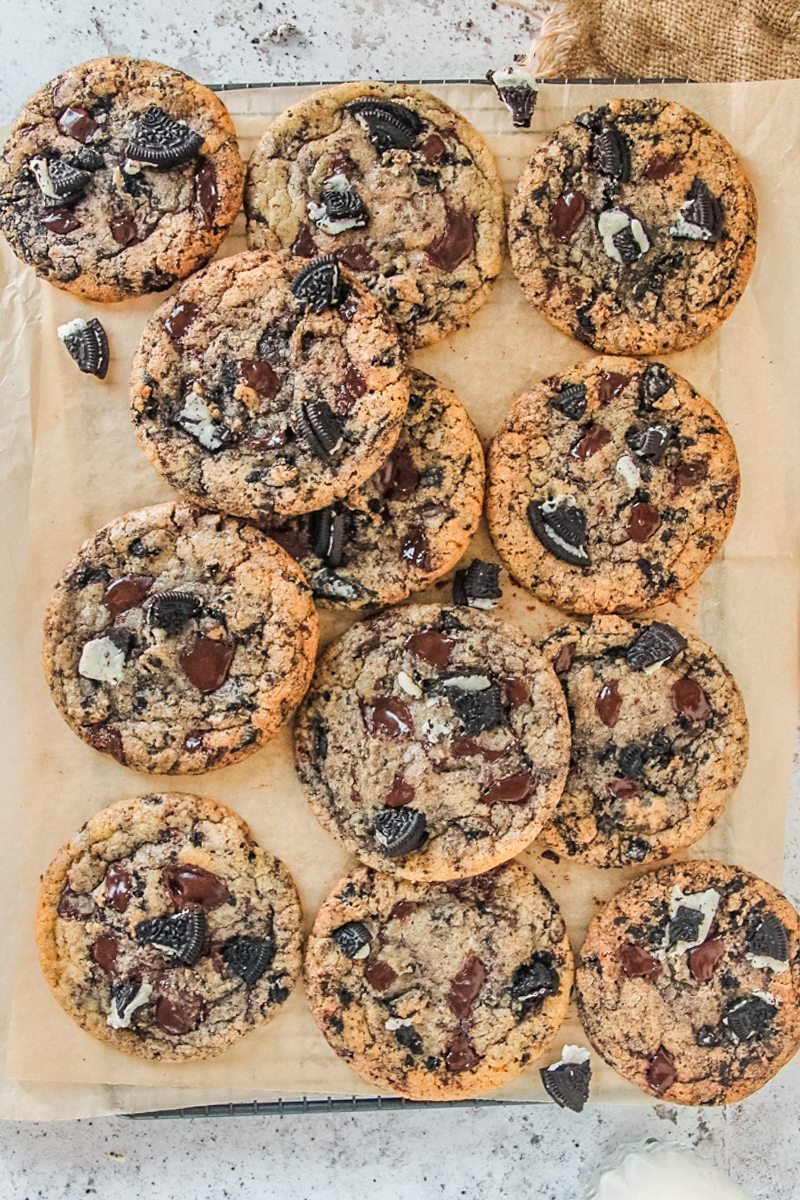 Oreo chocolate chip cookies is about to be picked up from a cooling rack lined with parchment paper on a light gray surface.