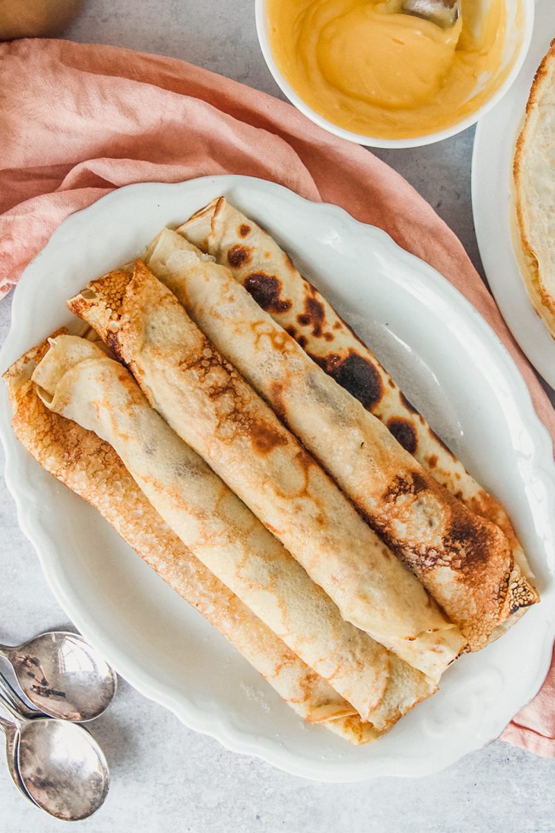 Filled rolled Spanish pancakes sit on an oval white ceramic plate on a gray surface.