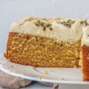 A slice of Passionfruit Cake sits on a serving plate on a cake stand on a gray surface.