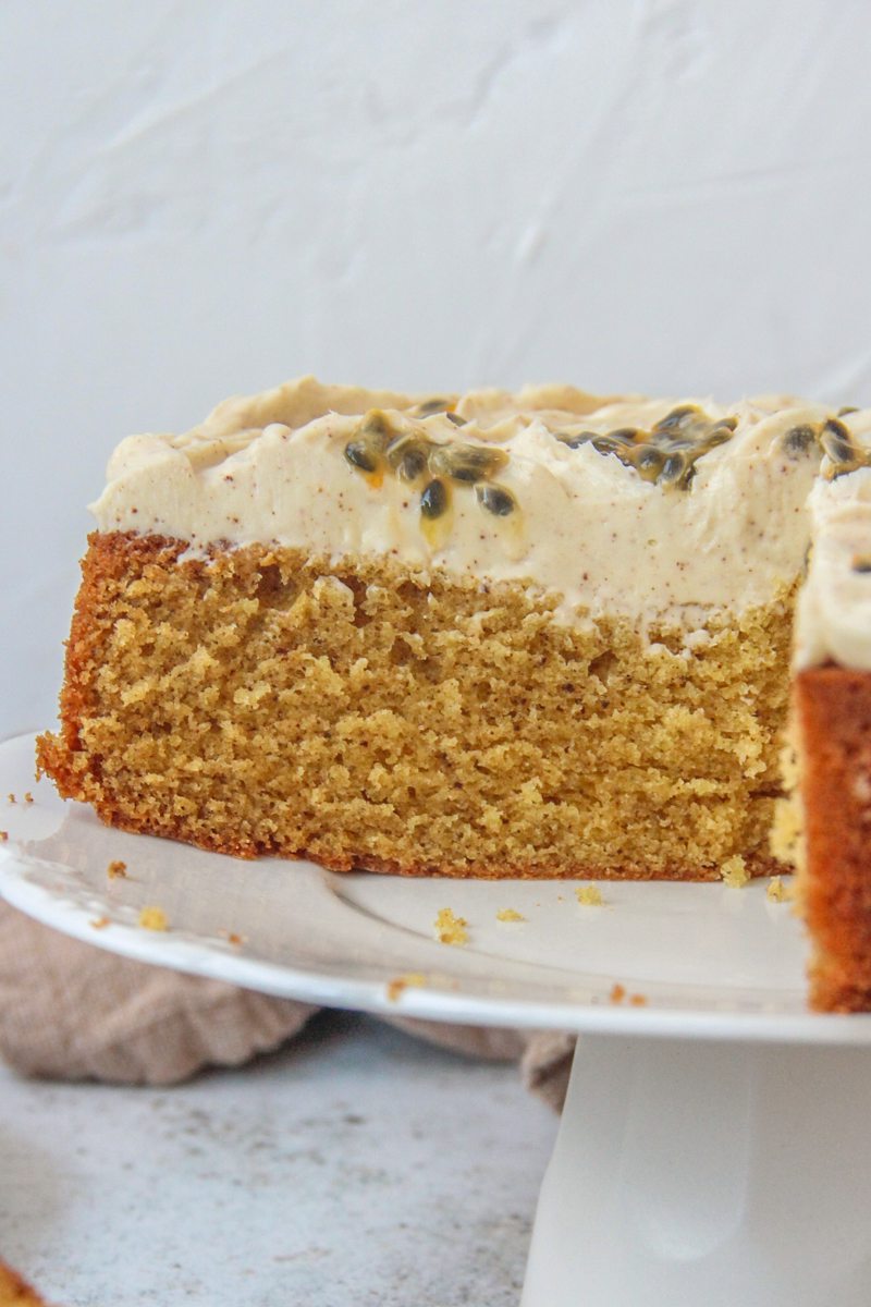 A slice of Passionfruit Cake sits on a serving plate on a cake stand on a gray surface.