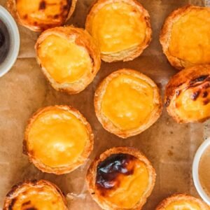 Pasteis de Natas or Portuguese Custard Tarts sit on parchment paper on a light gray surface.