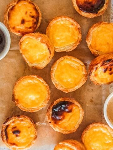 Pasteis de Natas or Portuguese Custard Tarts sit on parchment paper on a light gray surface.