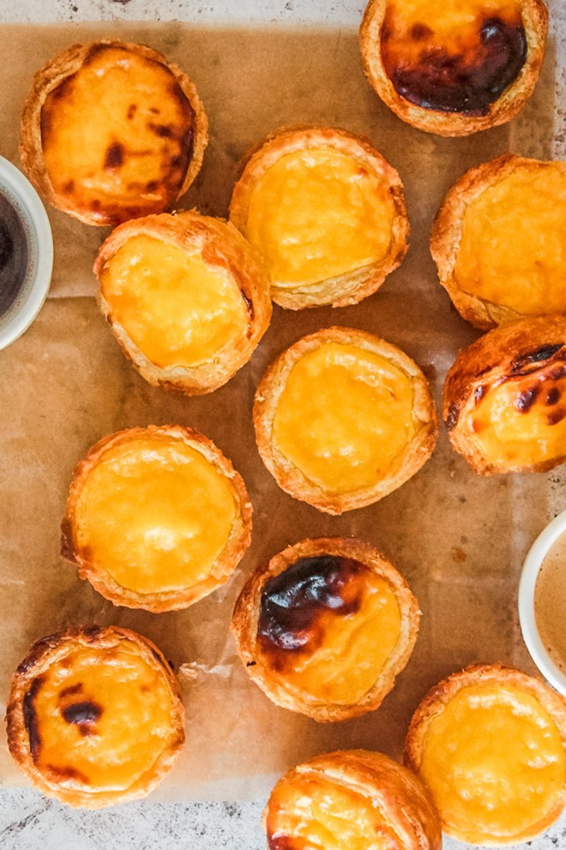 Pasteis de Natas or Portuguese Custard Tarts sit on parchment paper on a light gray surface.