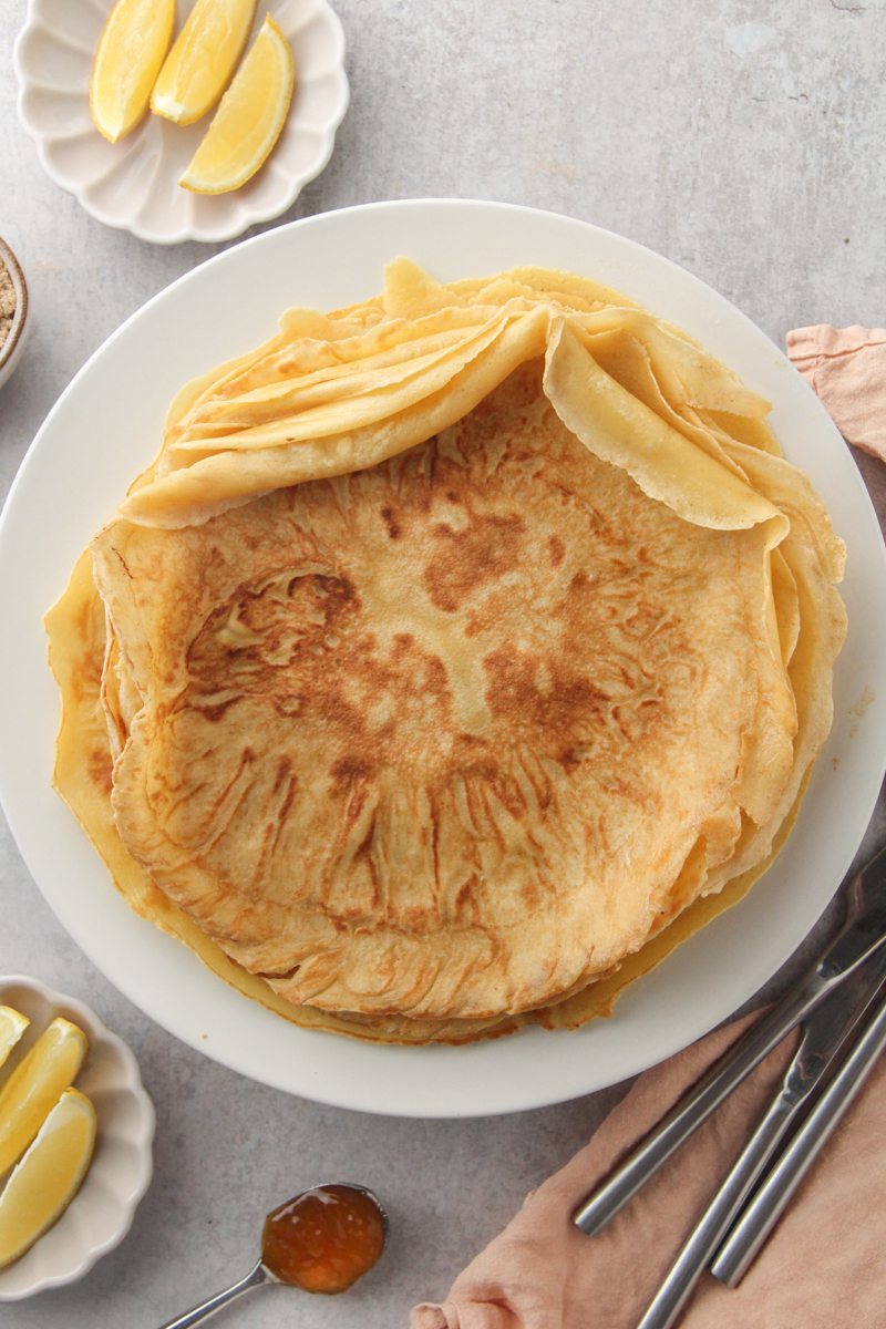 A stack of crepe style German Pancakes also known as Pfannkuchen on a white ceramic plate on a gray surface.