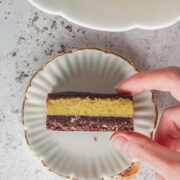 An individual pistachio custard bar is held on a small individual white ceramic plate with a golden rim on a light gray surface.