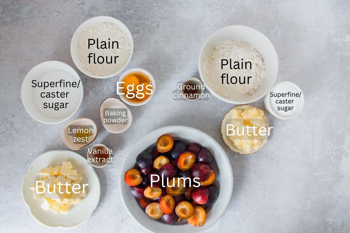 Ingredients for German Pflaumenkuchen or German Plum Cake sit in a variety of bowls on a gray surface.