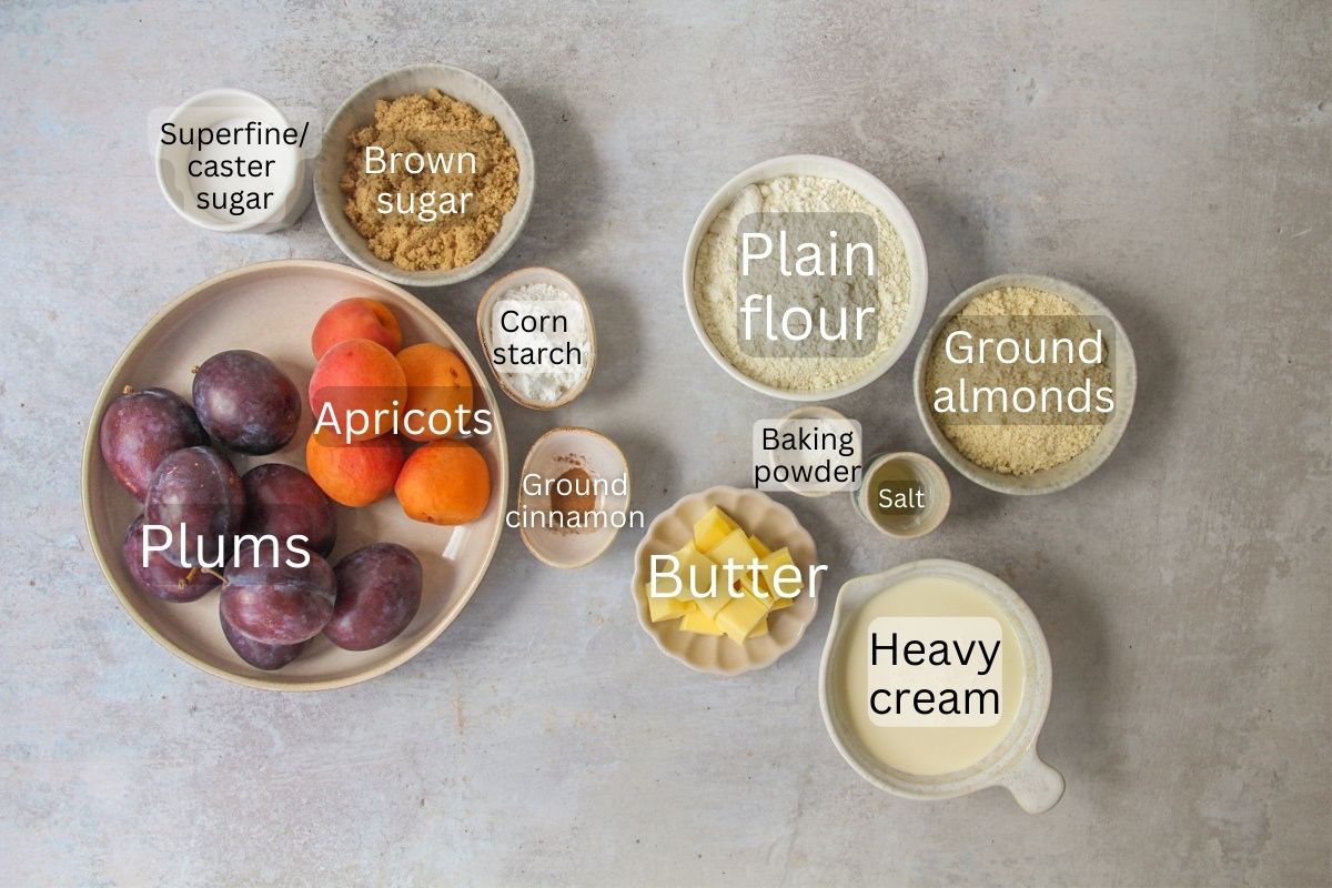Ingredients for Plum and Apricot Cobbler sit in a series of bowls on a gray surface.