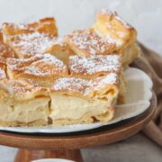 A close up of Karpatka slices sitting on a cake stand with a custard filling.