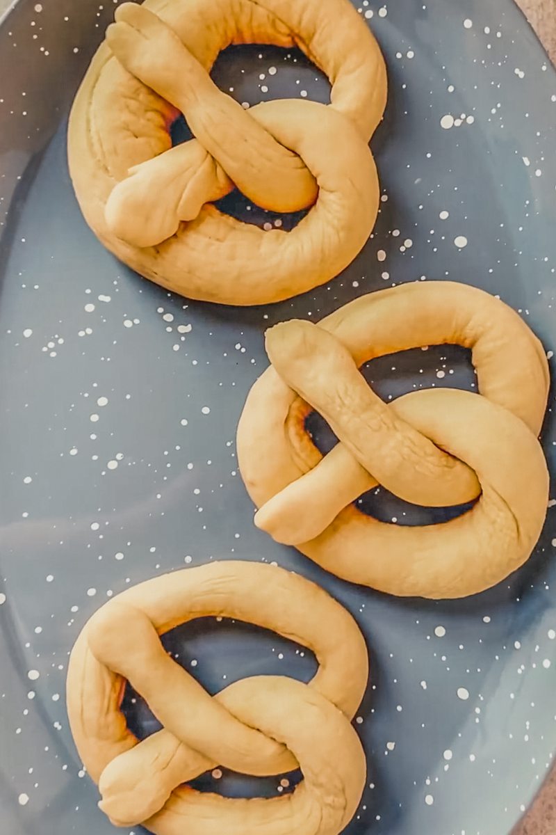 Unbaked pretzels sit on a speckled blue plate.