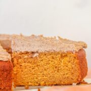 A slice of Pumpkin Cake with Coffee Buttercream sits on a cake server as the remaining cake sits on a cake stand.