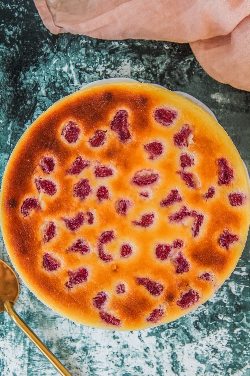 A raspberry custard cheesecake sits on a green and white speckled surface.