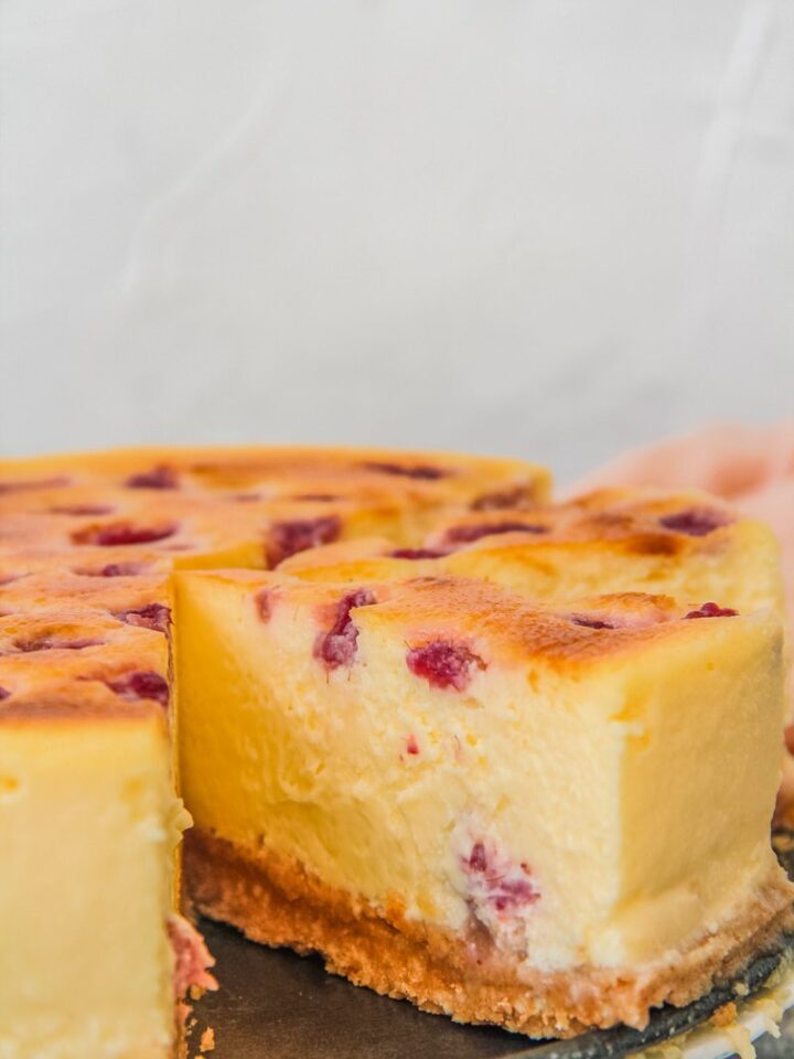 A slice of raspberry custard cheesecake sits beside the remaining cake.