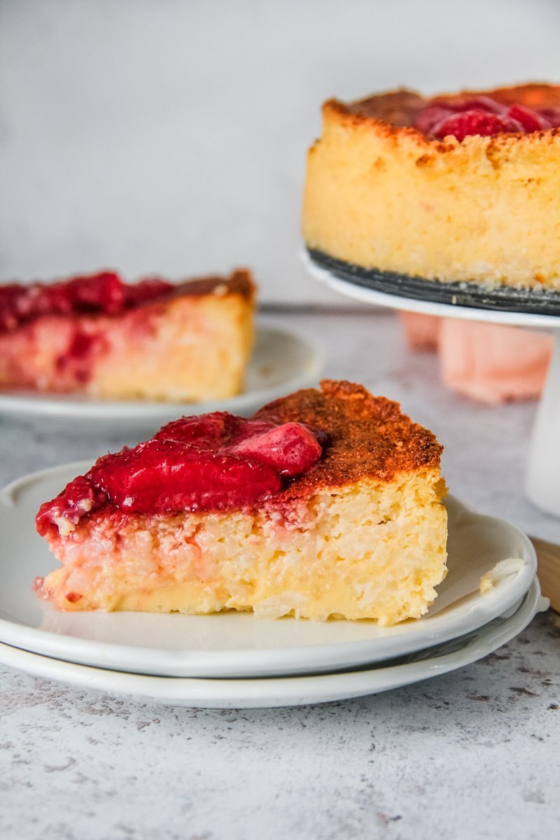 A slice of Hungarian rice pudding cake is served up on a stack of white plates on a light gray surface.