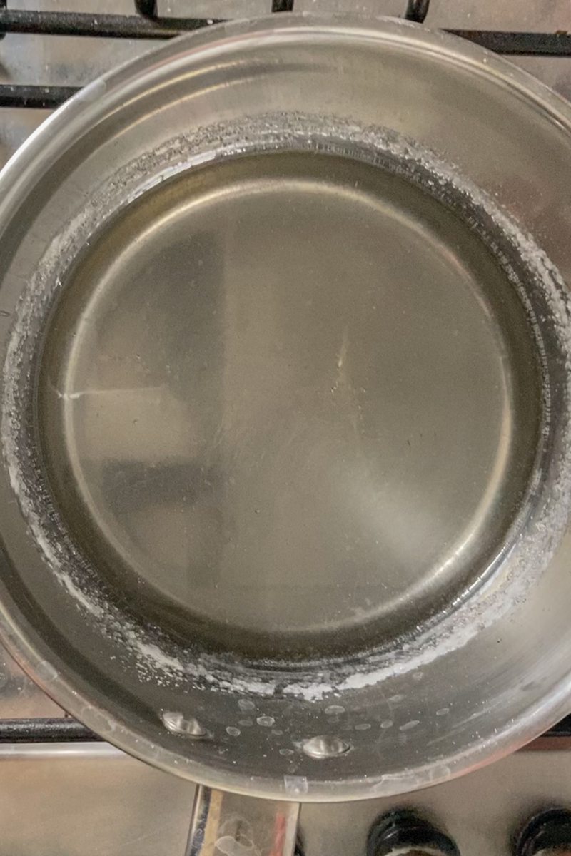 Sugar syrup sits in a stainless steel saucepan on a cooker.