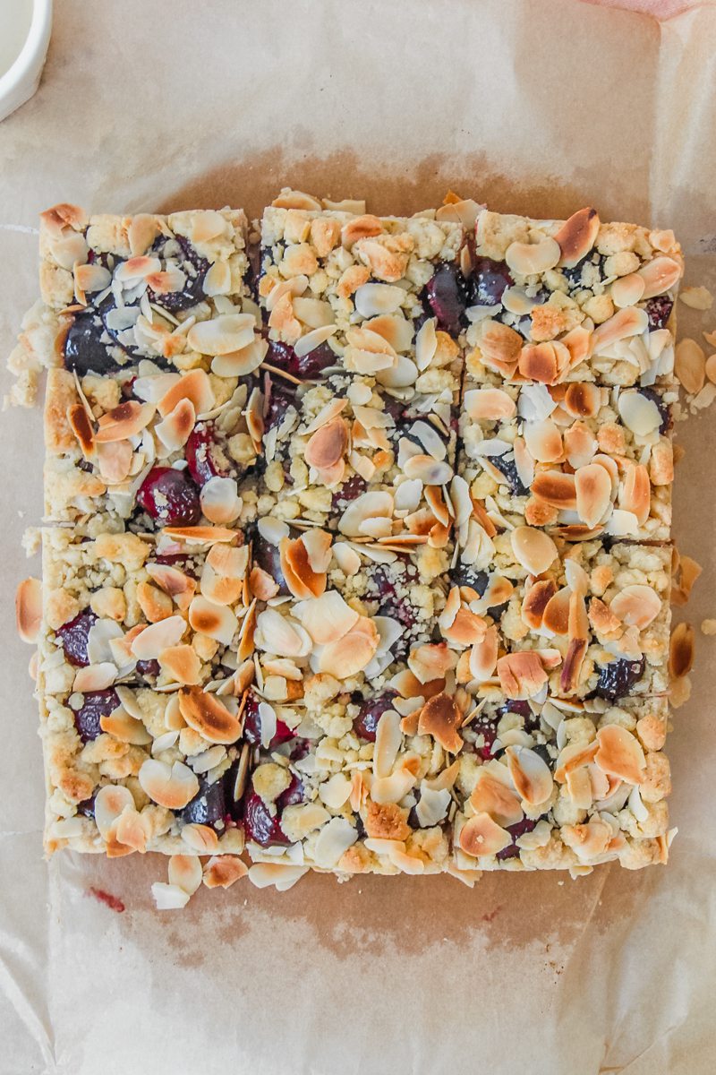 An overhead shot of Latvian Sweet Cherry Crumb Cake sits sliced up on parchment paper.