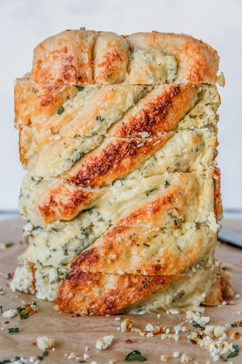 Sliced savory cheese babka sits on it's side with the layers of herbed cheese and brioche on a brown surface.