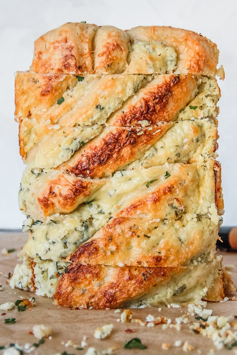 Sliced savory cheese babka sits on it's side with the layers of cheese and brioche on a brown surface.