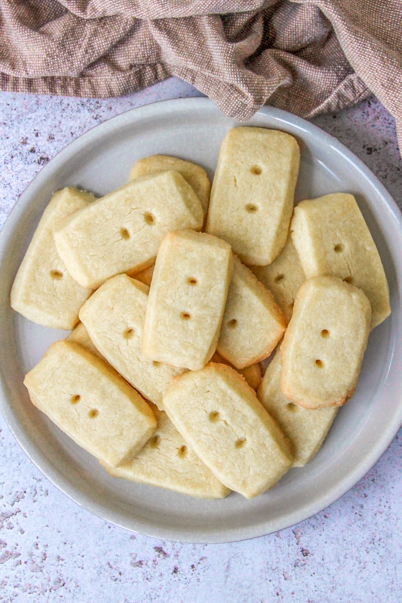 Shortbread sit on a deep plate on a gray surface with a brown cloth behind.