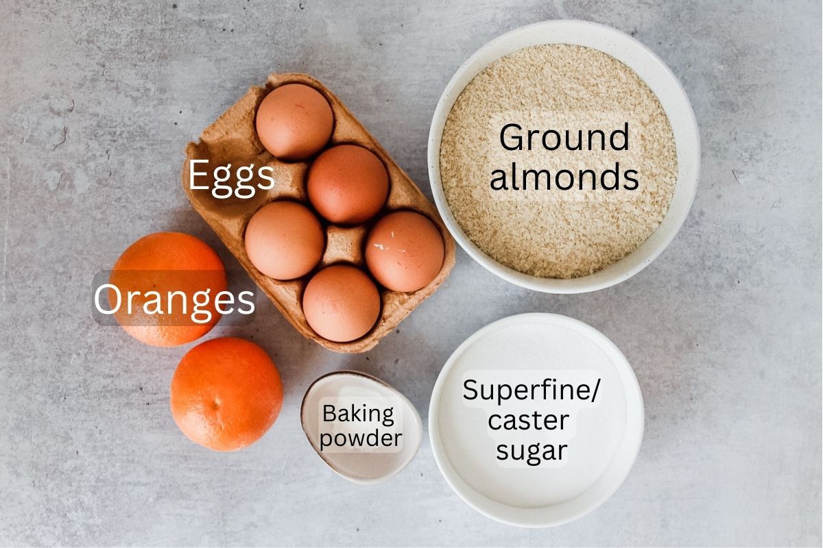 Ingredients for Sephardic Orange Cake sit in a series of bowls on a gray surface.