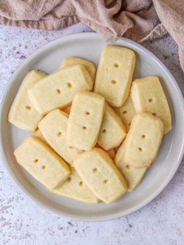 Scottish Shortbread sit on a deep plate on a gray surface with a brown cloth behind.
