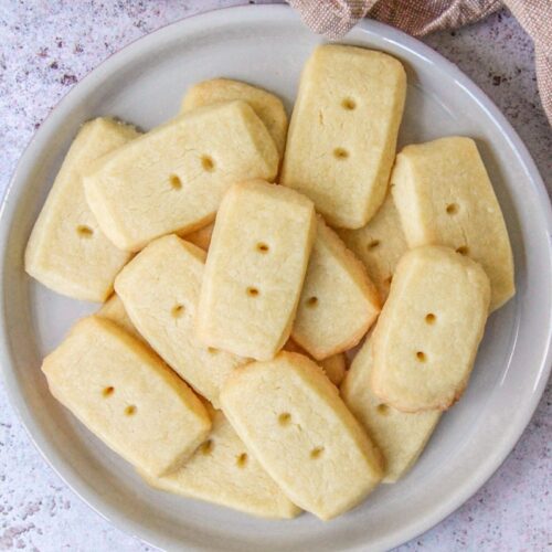 Scottish Shortbread sit on a deep plate on a gray surface with a brown cloth behind.