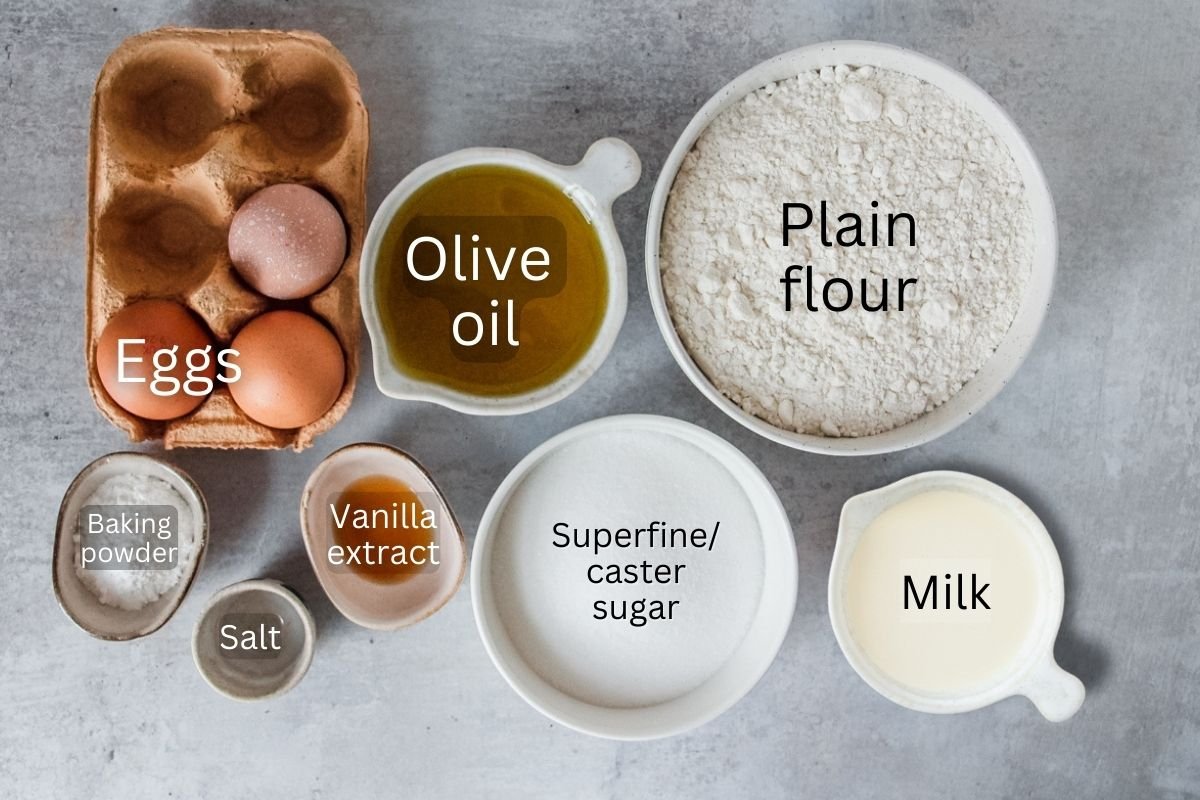 Ingredients for Spanish Olive Oil Cake sit in a variety of bowls on a gray surface.