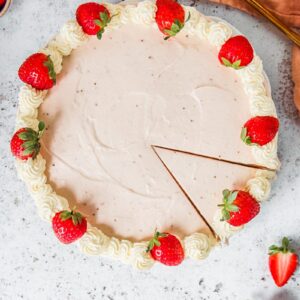 A no bake strawberry cheesecake topped with a whipped cream border and halved strawberries sits on a white plate on a light gray surface.