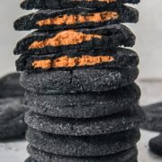 Stuffed black cocoa cookies stacked with a some split in half and the cookie butter centers visible; on a light gray surface.