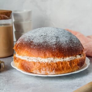 A Sufganiyot Cake or Donut cake sits on a white ceramic bowl on a gray surface.