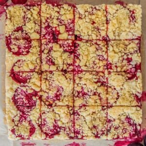 Svestkový tác - Czech Plum Cake sits on baking paper on a gray surface with 16 slices into the square cake.