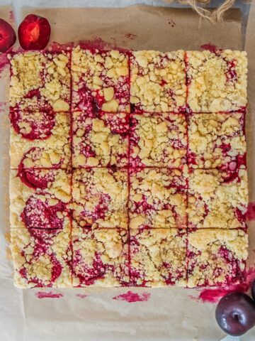 Svestkový tác - Czech Plum Cake sits on baking paper on a gray surface with 16 slices into the square cake.