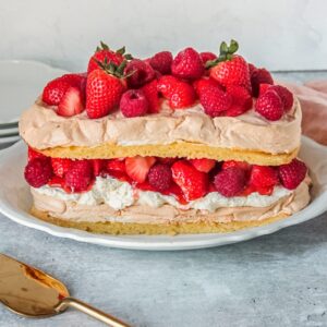 A Swedish meringue cake sits on an oval white ceramic plate on a gray surface.