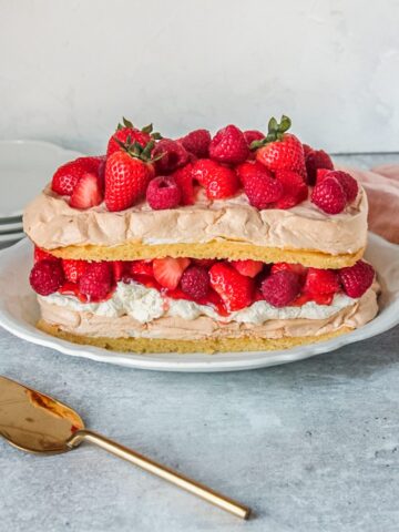 A Swedish meringue cake sits on an oval white ceramic plate on a gray surface.