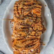 An overhead view of sweet potato babka with coffee glaze served up on a white oval plate with a few slices laying against the edges of the plate on a gray surface.