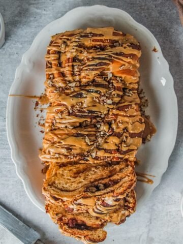 An overhead view of sweet potato babka with coffee glaze served up on a white oval plate with a few slices laying against the edges of the plate on a gray surface.