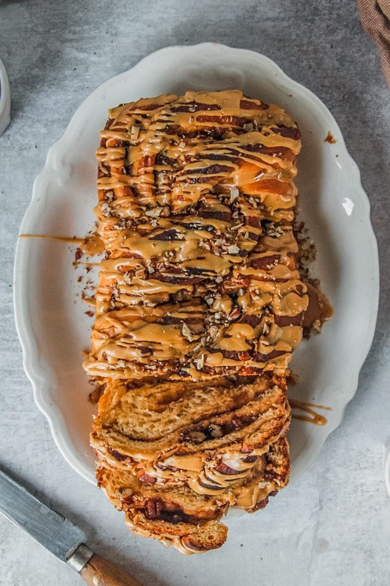 An overhead view of sweet potato babka with coffee glaze served up on a white oval plate with a few slices laying against the edges of the plate on a gray surface.