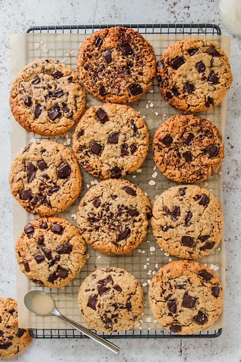 Tahini oatmeal cookies with chocolate chunks sit on top of a lined cooling rack on a light gray surface.