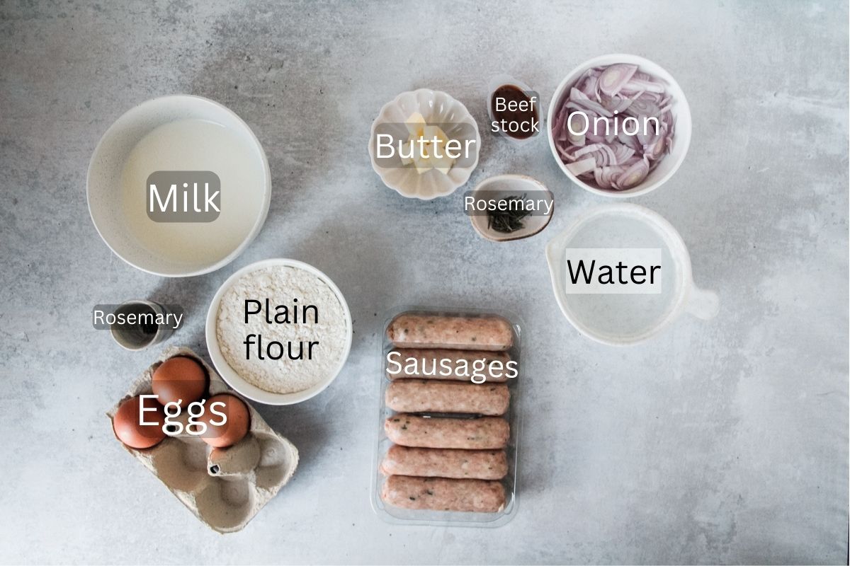 Ingredients for Toad in a Hole sit in a variety of bowls and plates on a gray surface.