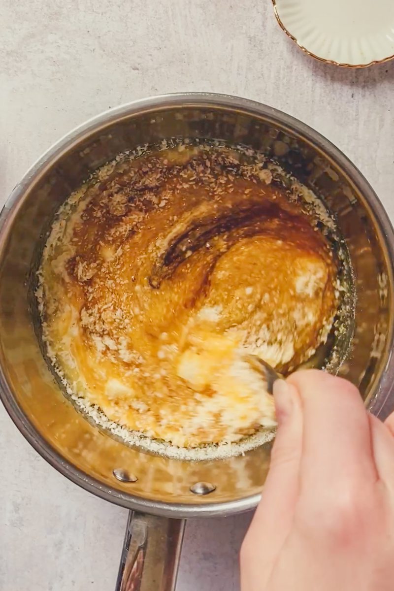 The filling for treacle tart is stirred in a stainless steel saucepan on a gray surface.