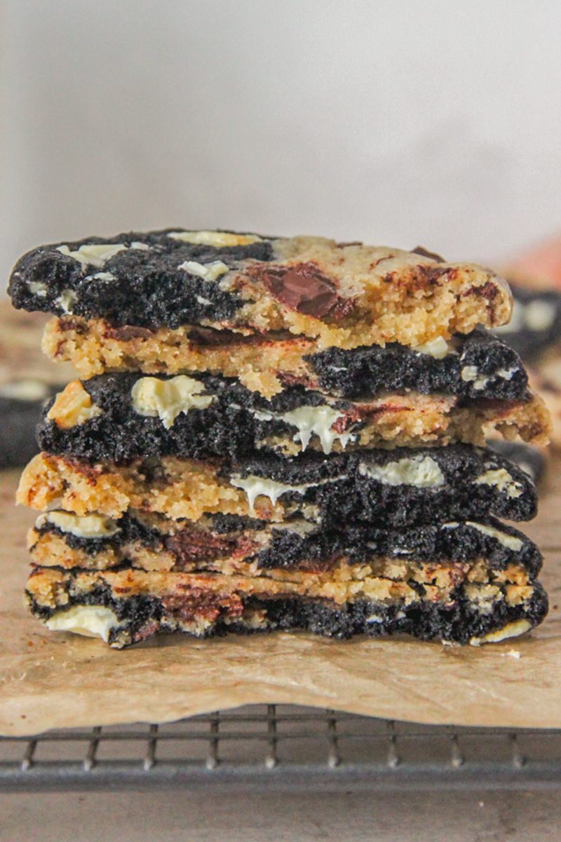 Triple chocolate cookies sit halve and stack on each other with the two sides visible and melting chocolate chunks sits on brown paper.