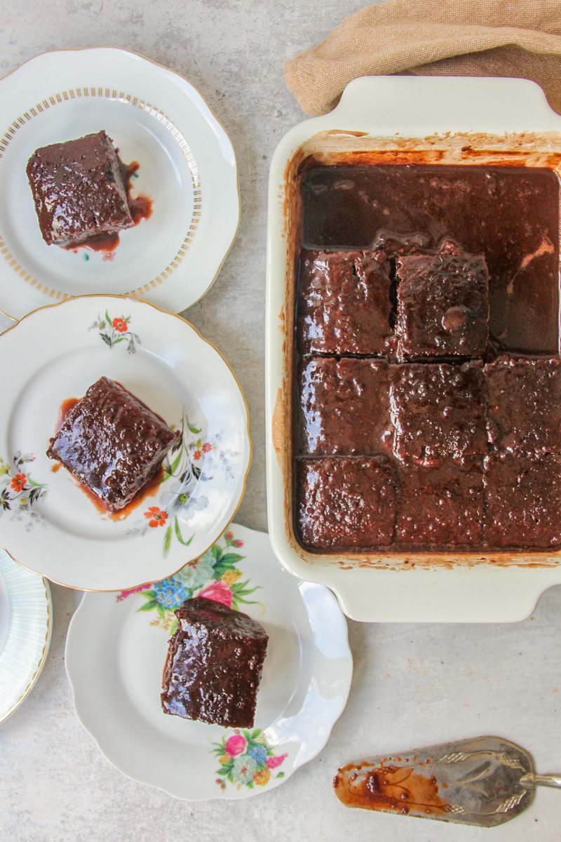 Turkish Chocolate Sauce Cake sits on a gray surface with some individual slices on individual plates.