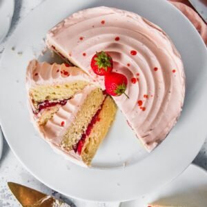 An overhead image of slices of two layer Vanilla Cake filled with roasted strawberries and coated in a strawberry buttercream; on a light grey background.