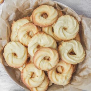 Vanillekranse - Danish butter cookies sit in a deep ceramic plate lined with parchment paper on a gray surface with tea beside.