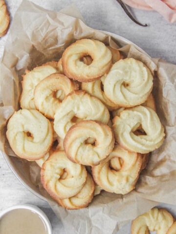 Vanillekranse - Danish butter cookies sit in a deep ceramic plate lined with parchment paper on a gray surface with tea beside.