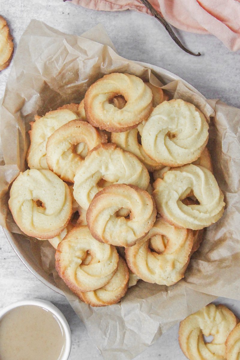 Vanillekranse - Danish butter cookies sit in a deep ceramic plate lined with parchment paper on a gray surface with tea beside.