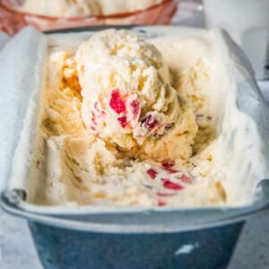 Scoops of cherry white chocolate no churn ice cream sit on top of a lined rectangle metal tin on a light gray surface.
