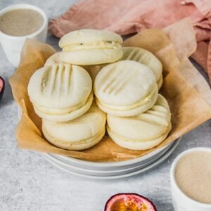 A stack of melting moments sit on a stack of rimmed ceramic plates on a gray surface.