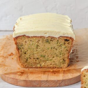 A sliced zucchini loaf cake sits on a parchment lined wooden board on a gray surface.
